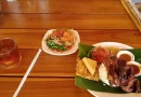 Ilustrasi sajian ayam bakar bumbu rempah dan sate daging khas daerah di atas piring tradisional.