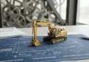 Miniatur eksavator kuning di atas maket biru kawasan industri hijau yang bersih dan modern.