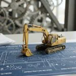 Miniatur eksavator kuning di atas maket biru kawasan industri hijau yang bersih dan modern.