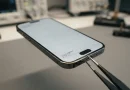 Seseorang sedang memeriksa kondisi fisik smartphone bekas berwarna hitam secara teliti.