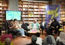 Ilustrasi buku terbuka berdampingan dengan piringan hitam dan alat musik berlatar hangat